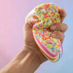 Hand squeezing a rainbow cake slice squishy toy