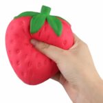 Hand squeezing a red strawberry squishy toy